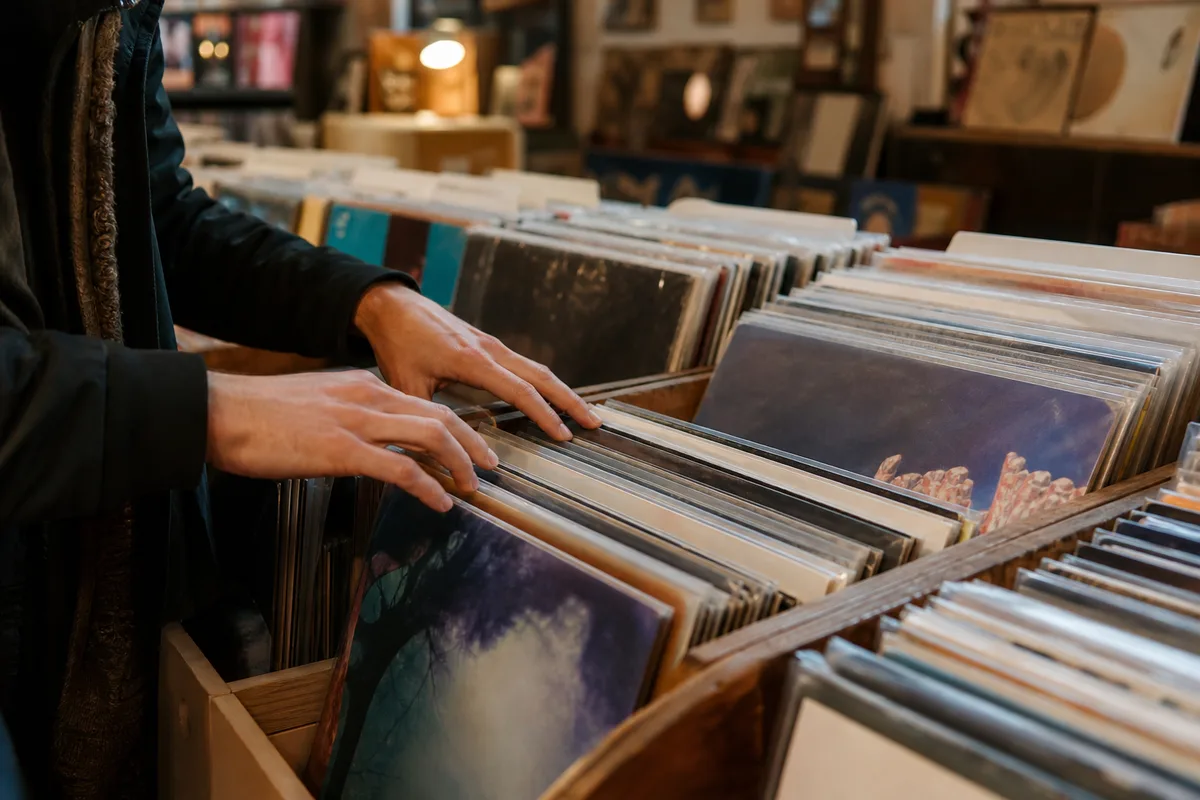 Bacs de disquaire remplis de pochettes de vinyles, mains feuilletant les disques dans une boutique