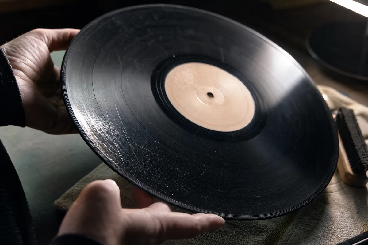 Mains examinant un disque vinyle noir incliné sous une lumière rasante pour repérer les rayures