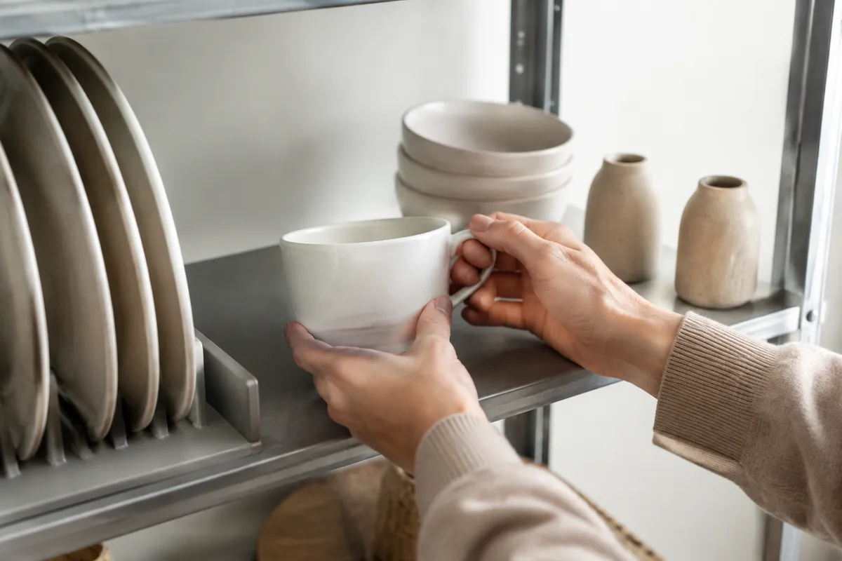 Mains rangeant des tasses et des assiettes propres sur une étagère métallique dans une réserve claire