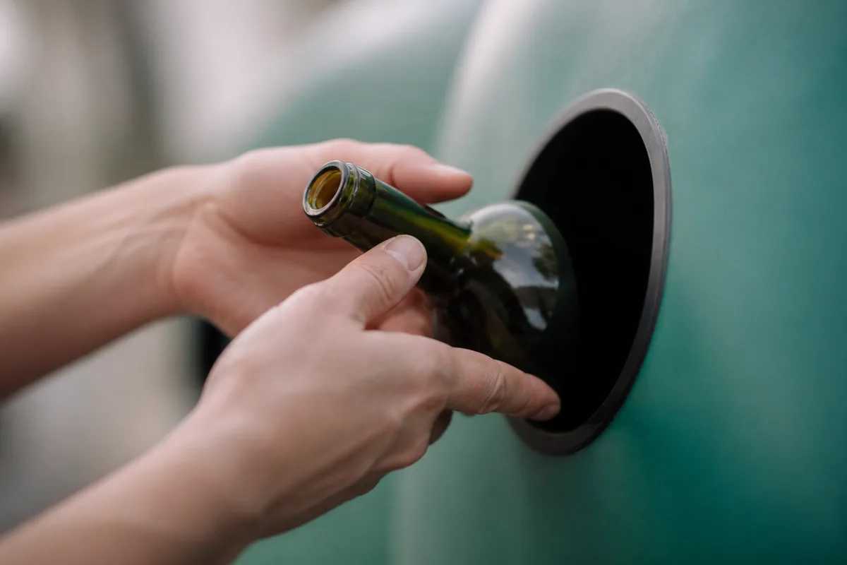 Mains déposant une bouteille en verre teinté dans l’ouverture ronde d’un conteneur